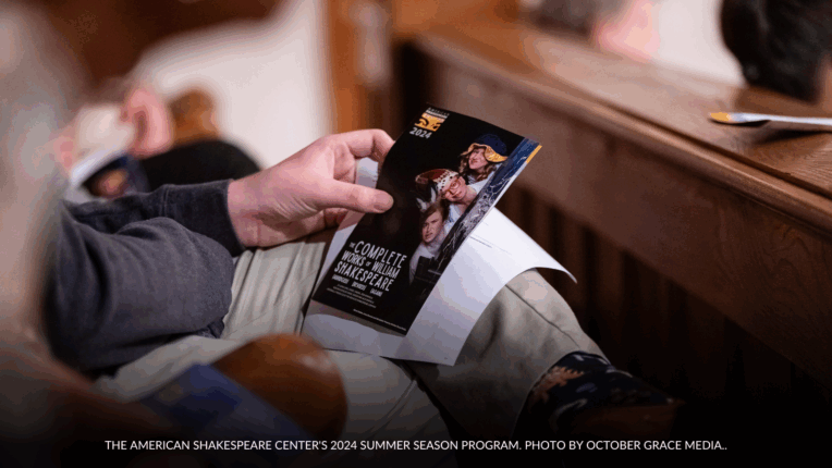 An audience member holds the American Shakespeare Center’s printed show program for the 2024 Summer Season while seated inside the Blackfriars Playhouse. Caption reads: The American Shakespeare Center's 2024 Summer Season Program. Photo by October Grace Media.
